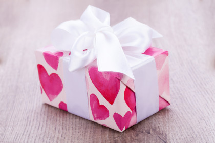 Pretty Valentines gift with hearts on the giftwrap on a big white ornamental bow on top, closeup high angle view of a gift for a loved one or sweetheart